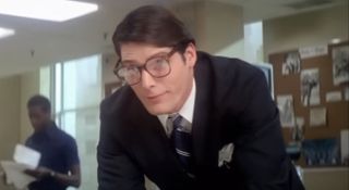 Christopher Reeve leans over a table while dressed as Clark Kent in Superman II.