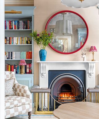 Colorful living room with blue painted alcove shelving, red rounded mirror above marble fireplace, checkered armchair