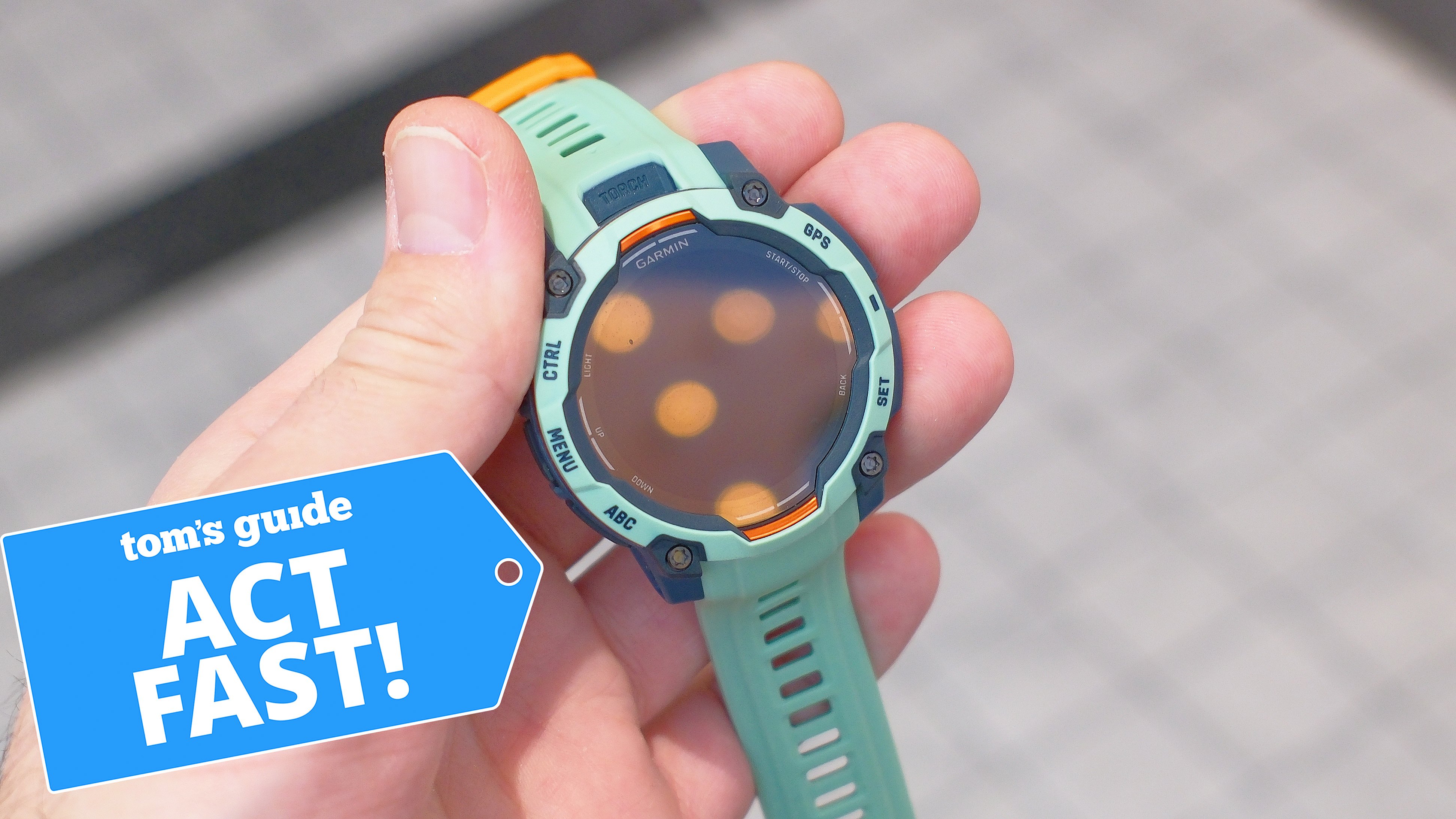 Garmin Instinct 3 in teal in a user's hand next to a deals badge