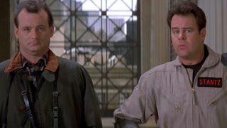 Bill Murray in a green coat with a brown collar, standing next to Dan Aykroyd in his Ghostbuster uniform as they walk into the museum in Ghostbusters II. 