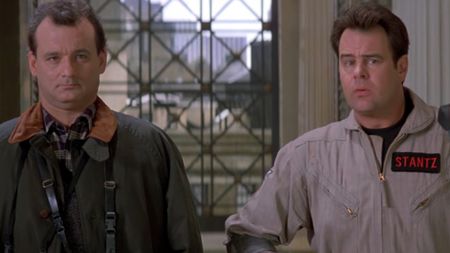 Bill Murray in a green coat with a brown collar, standing next to Dan Aykroyd in his Ghostbuster uniform as they walk into the museum in Ghostbusters II. 