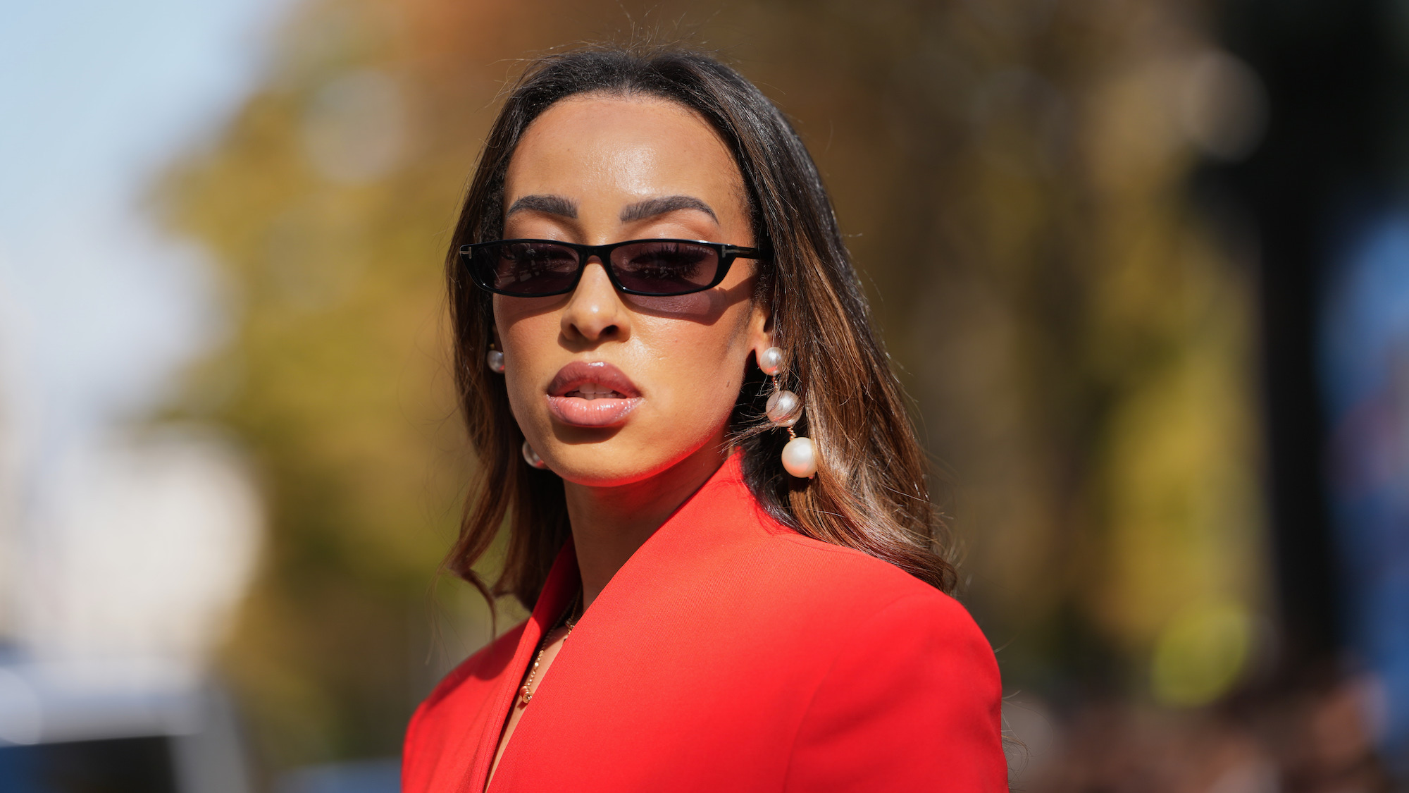 Woman wearing sunglasses with brunette hair, pearl earrings and red jacket - SPF with benefits