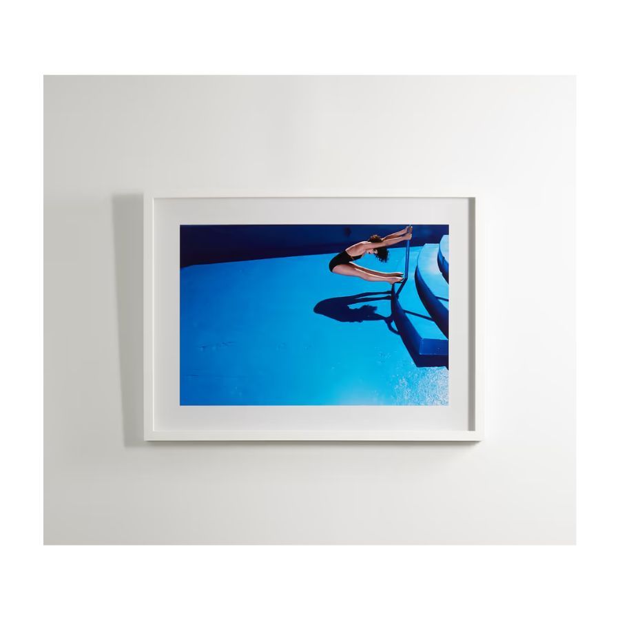 Photograph of blue swimming pool and woman holding onto stairs rail