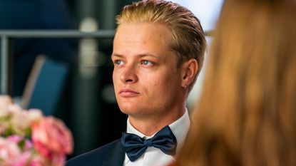 A shoulders-up shot of Marius Borg Høiby wearing a tuxedo sitting at a table with a floral centerpiece