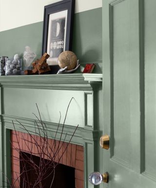 close up of fireplace painted mid-green, decor on top with black frame with picture, door painted the same green