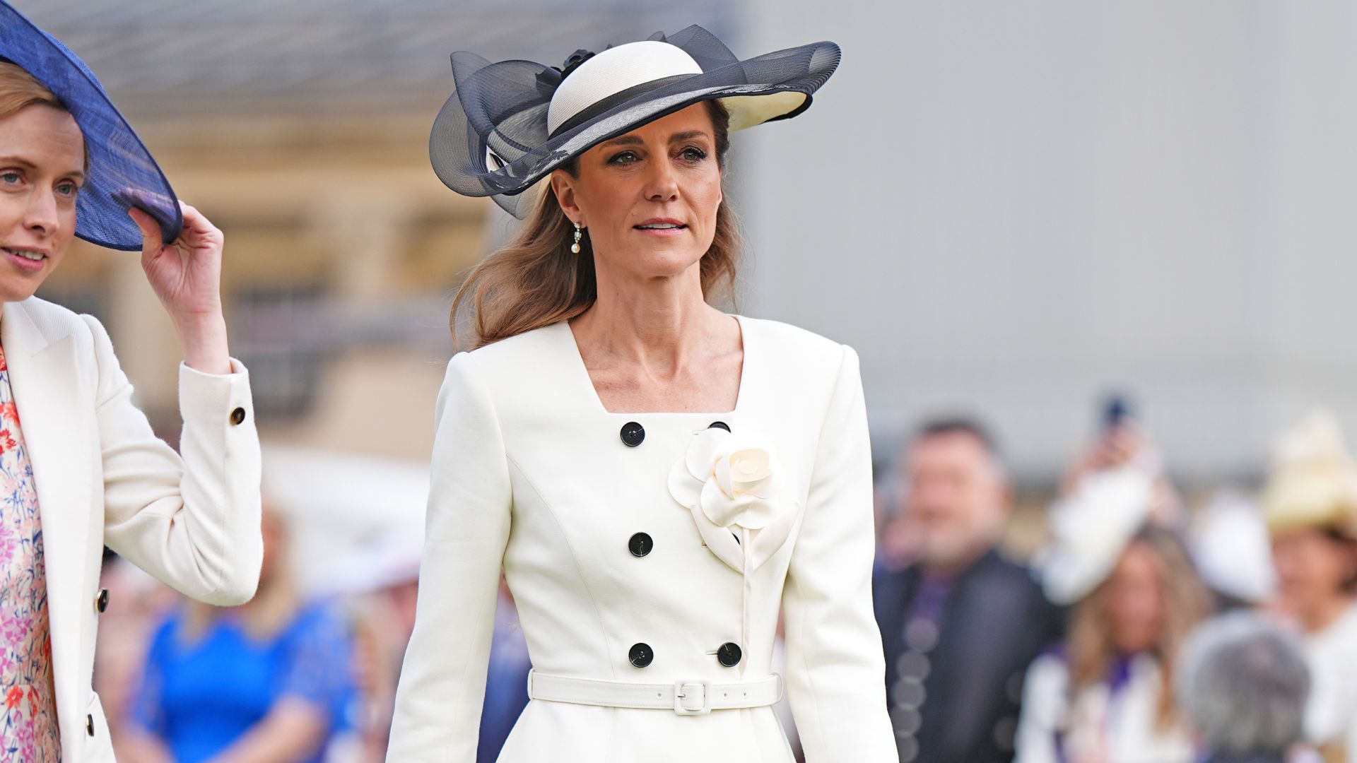 Kate Middleton wears a pleated polka-dot skirt with a white peplum jacket and beige heels.
