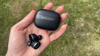 Bowers & Wilkins Pi8 earbuds, held in a hand on grassy background