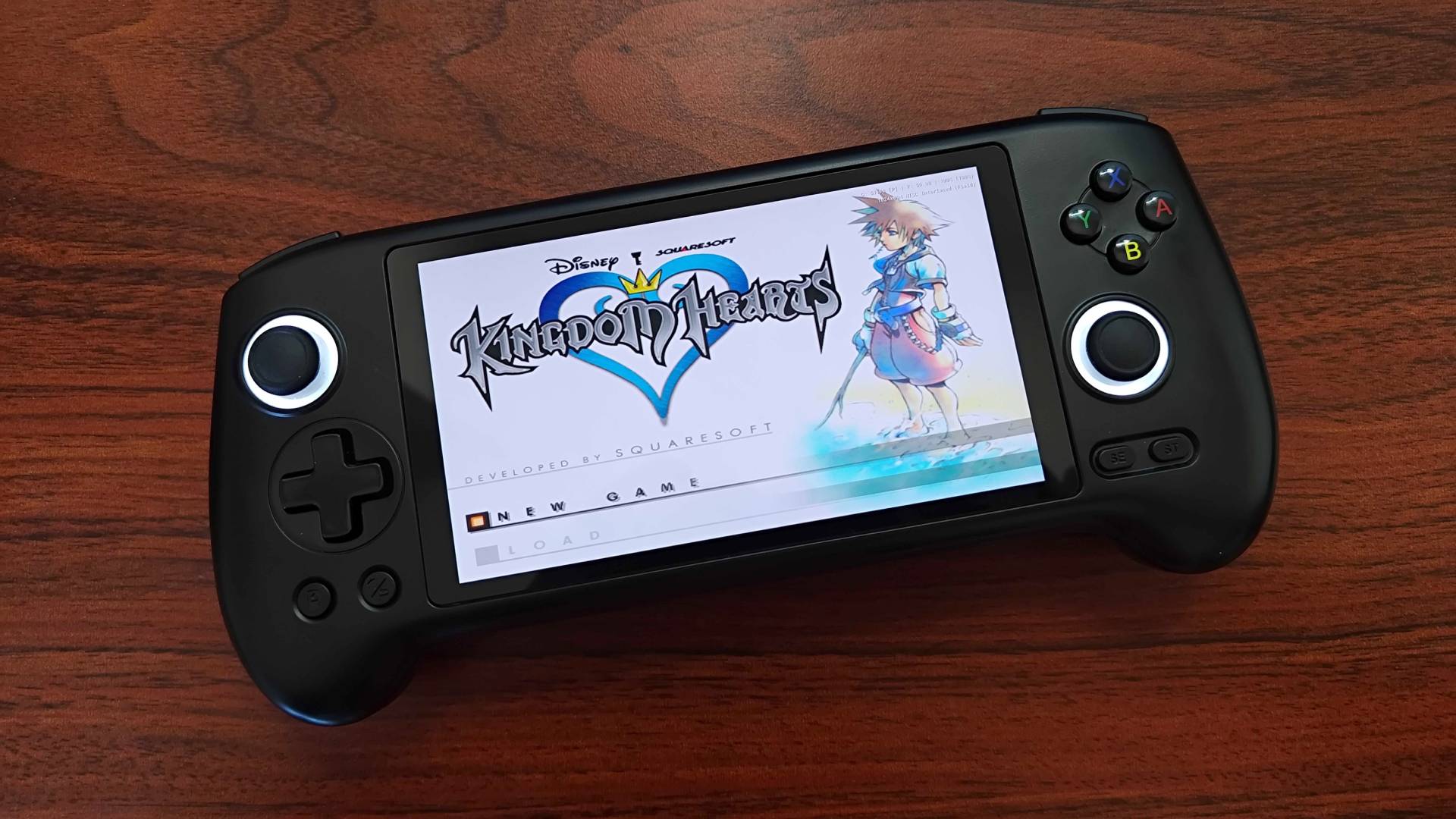 Anbernic RG556 handheld on woodgrain desk with Kingdom Hearts menu screen displayed.