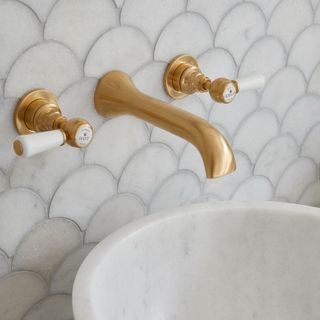 Gold wall mounted taps, hot and cold handle eitherside of a solo mixer, above a white basin