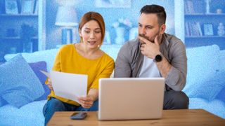 Couple looking at bills whilst sitting on a sofa, in front of a laptop