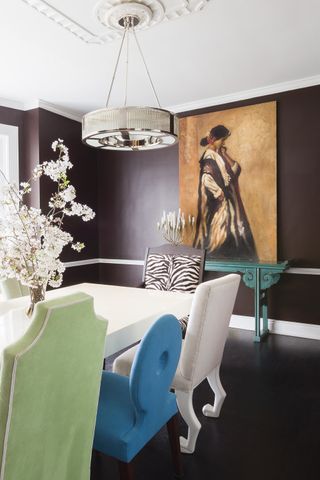 chocolate brown dining room with chair rail, artwork, white dining table, pendant light, mismatched chairs