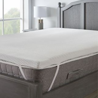 A memory foam mattress topper on a mattress on a grey upholstered bed