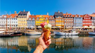 A hand holds an ice cream cone against the backdrop of boats and homes in Denmark.