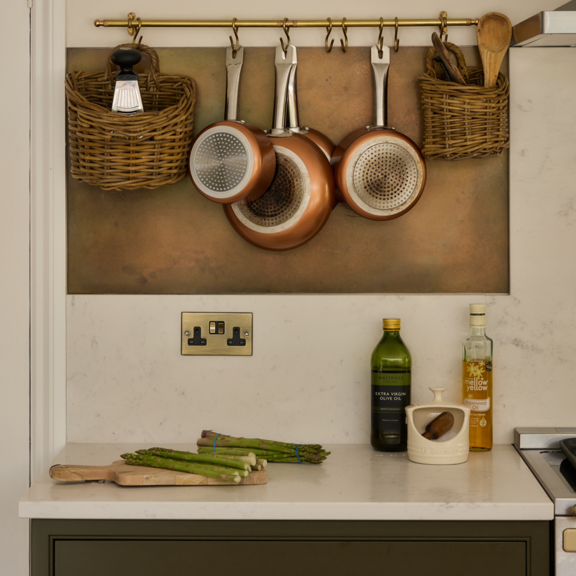 kitchen detail with brass hanging rail with saucepans and baskets hanging above a white work top with olive oils