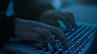 Insider threat hacker concept image showing man typing on keyboard in a dimly lit room. 