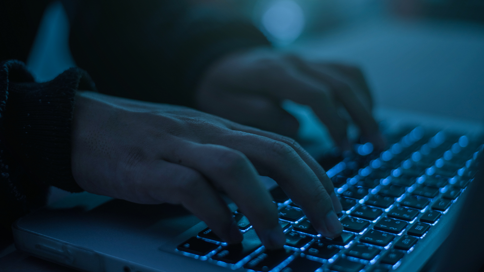 Insider threat hacker concept image showing man typing on keyboard in a dimly lit room. 