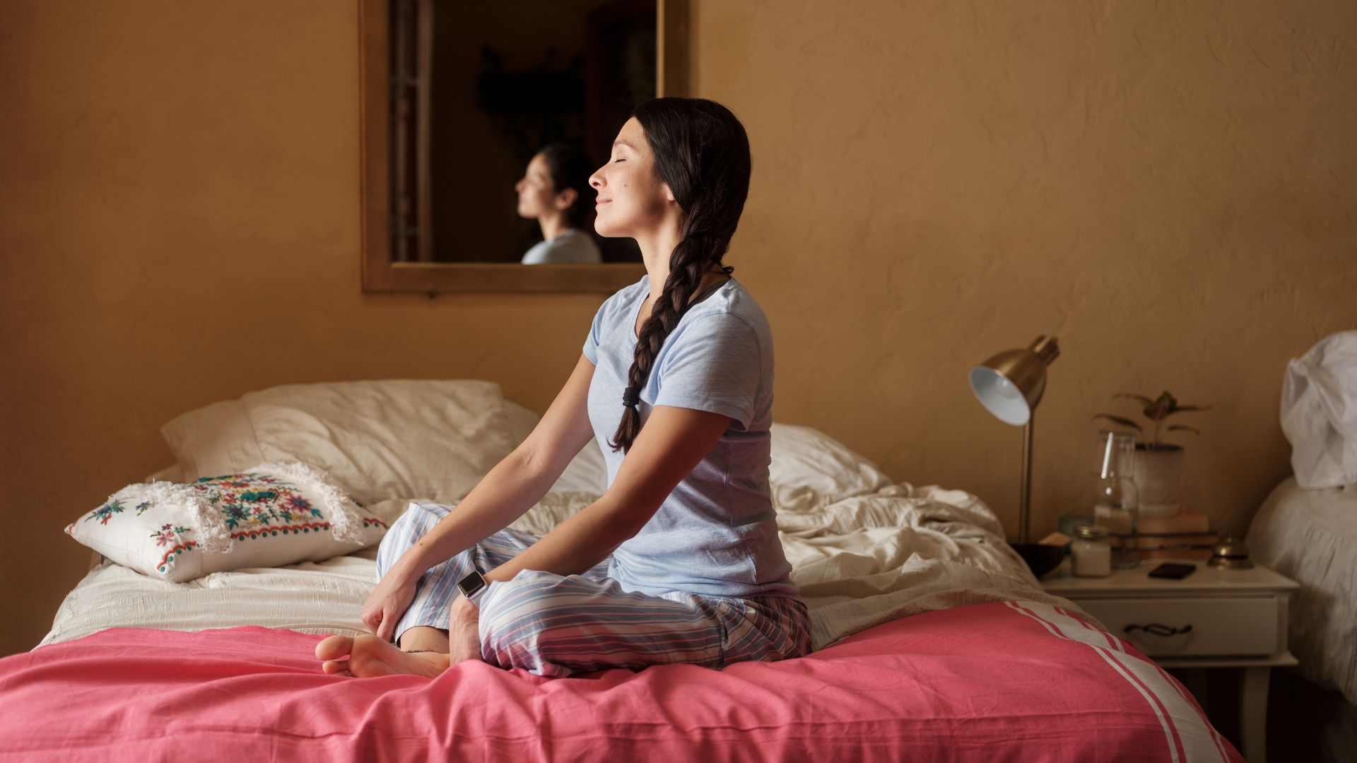 A woman sits cross-legged on her bed with her eyes closed.