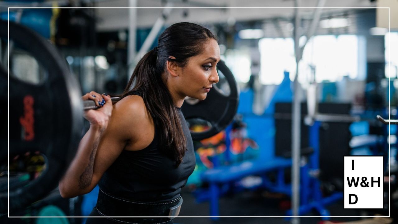 Poorna Bell holding barbell over her shoulders, looking ahead