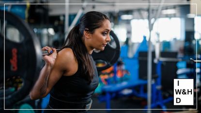 Poorna Bell holding barbell with weights on it over her shoulders, looking ahead