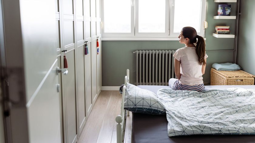 A brunette woman with a ponytail sitting on the bed of her childhood bedroom.