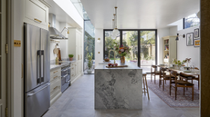 large, light filled kitchen extension with waterfall marble counter, shaker cabinets and a glass wall out to the garden