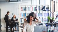 Software developer burnout concept image showing female programmer sitting at a desk looking stressed.