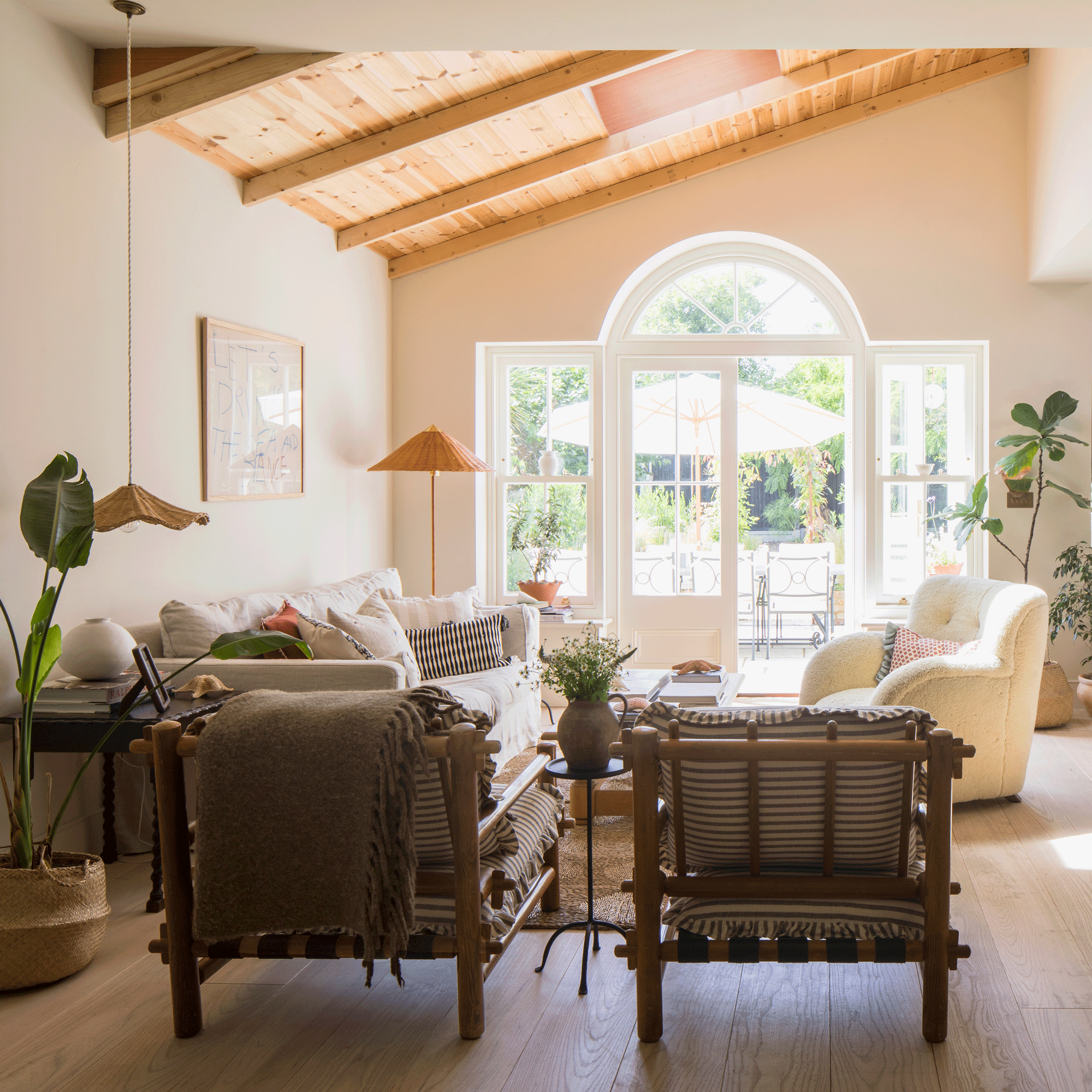 a large neutral living area with patio doors cream sofas and wooden armchairs, and a wooden clad ceiling