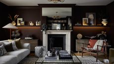 Image of a chocolate brown living room with a fireplace in the center of the room. There is a an off-white sofa and rug with a glass coffee table in the center.