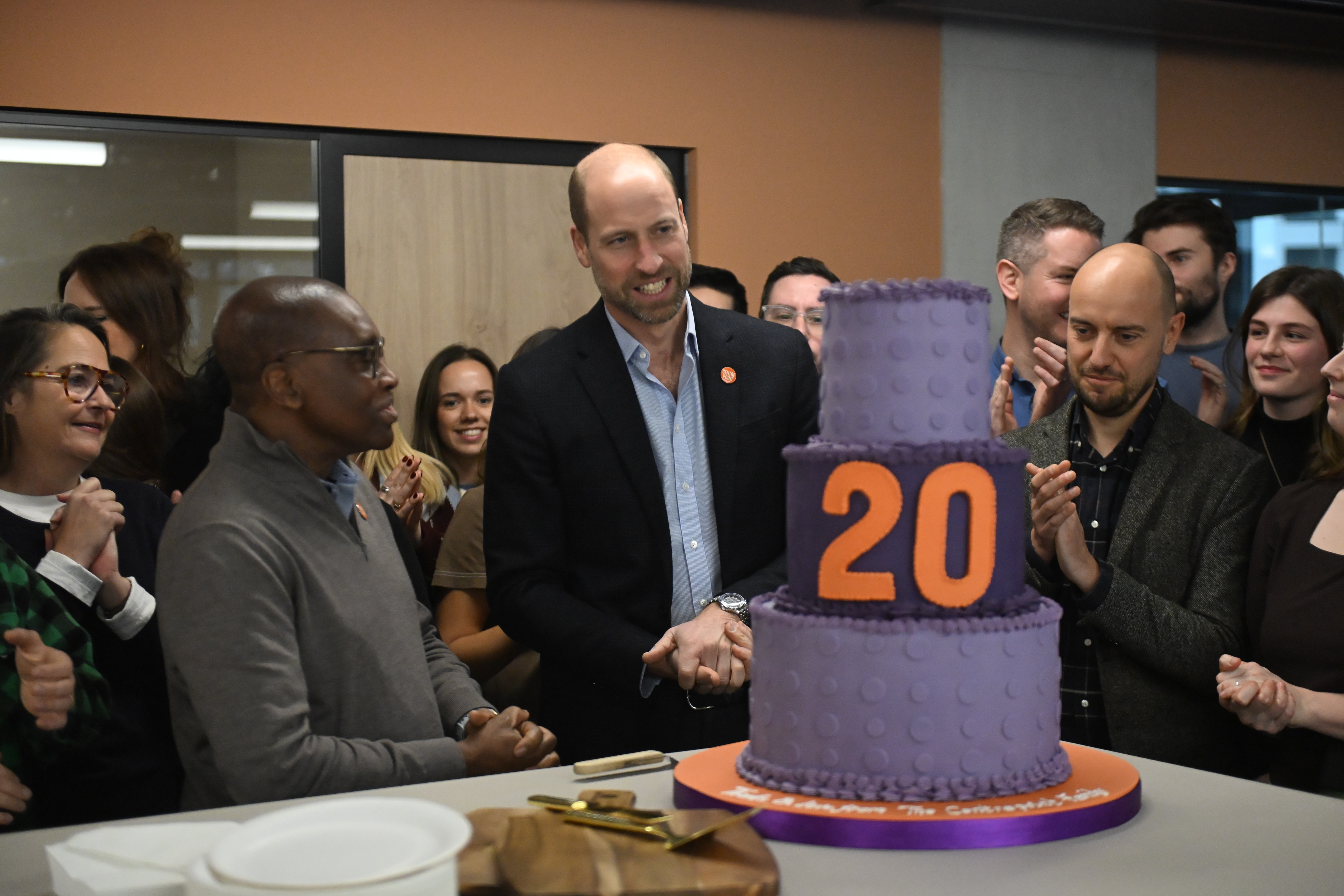 Prince William standing in front of a purple cake reading &quot;20&quot;