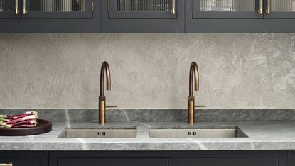 a kitchen with a grey worktop with antiqued brass quooker taps