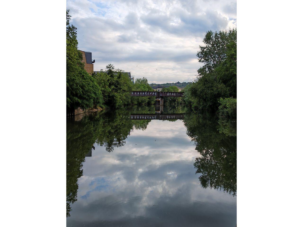 A bridge crossing a river that reflects the cloudy sky.