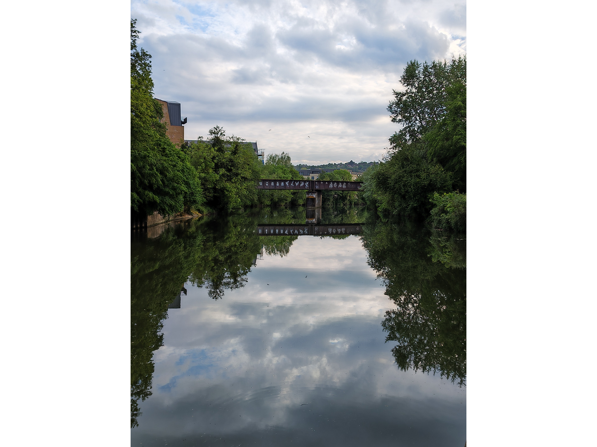 A bridge crossing a river that reflects the cloudy sky.