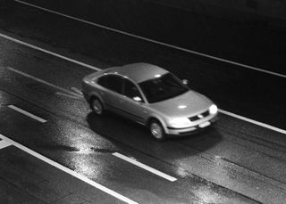 A black & white photo of a car driving down a road.