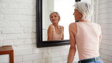 Woman looking in the bathroom mirror with reflection, representing how to stop thinning hair 