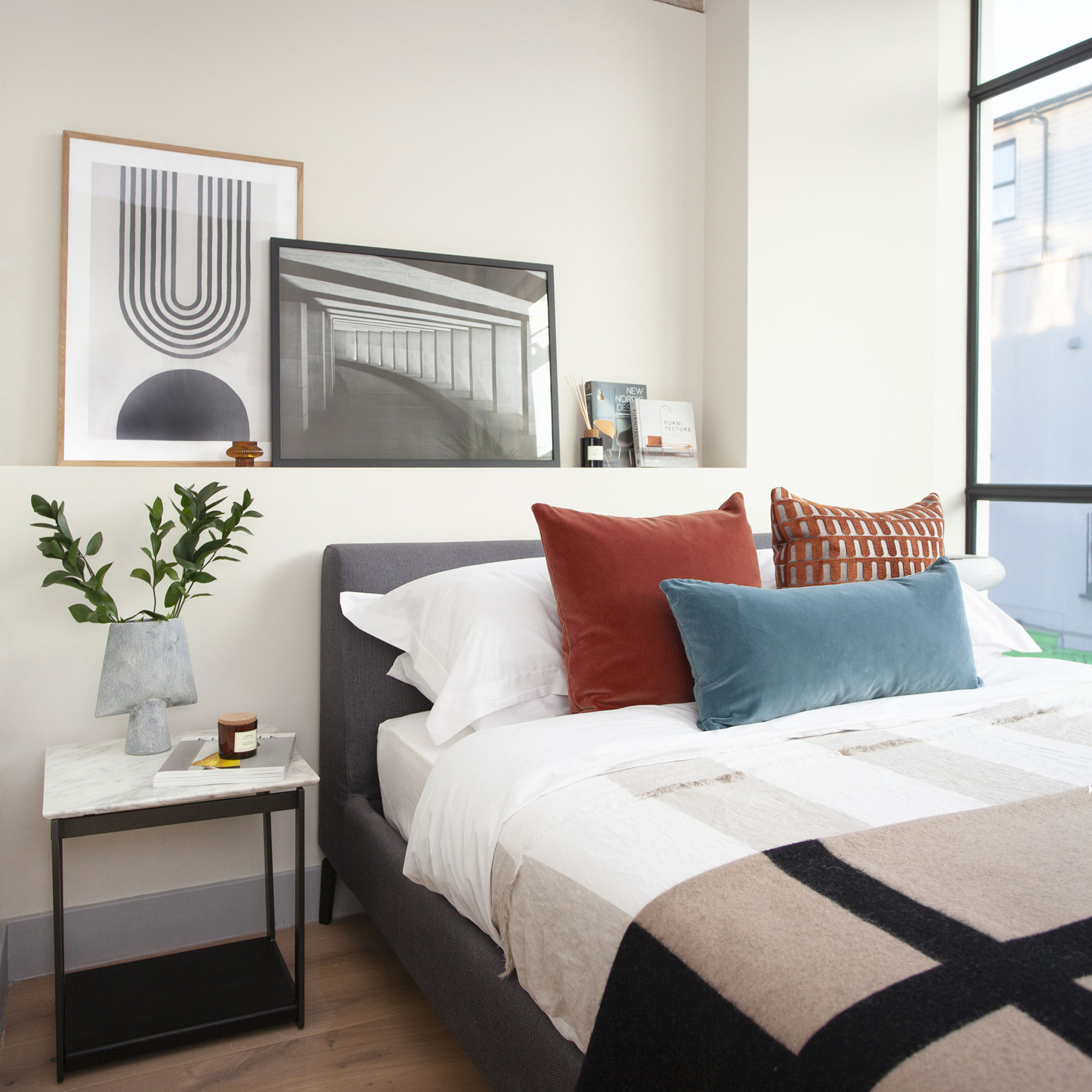 Cream bedroom with artwork on ledge and bed dressed with cushions and geometric throw