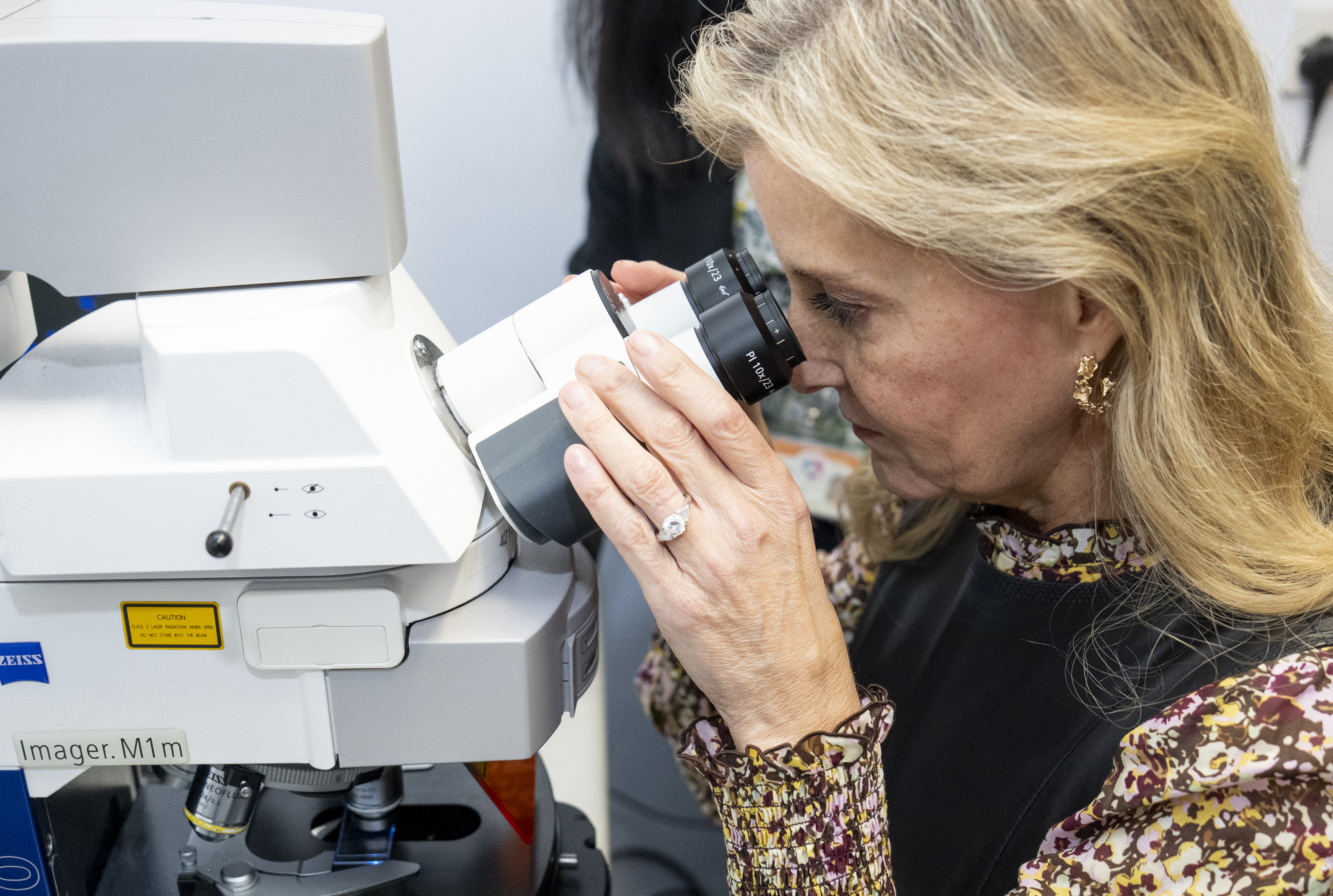 Duchess Sophie using a microscope, wearing a floral long sleeve dress