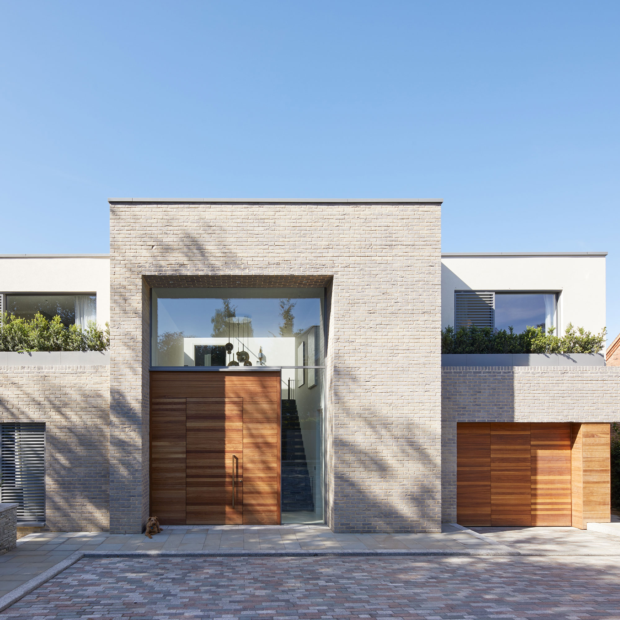 contemporary white brick house with wooden oversized front door and pale block paving