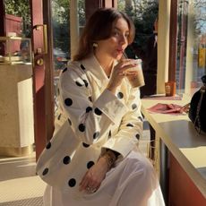 Woman wears polka dot trench coat, white skirt, gold jewellery