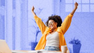 Young woman sitting at a table, looking excited and throwing her hands in the air.