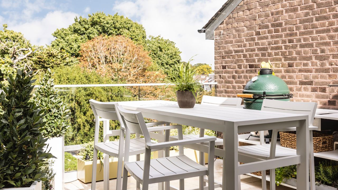 balcony with white furniture and outdoor kitchen, big green egg BBQ, planters, view of garden