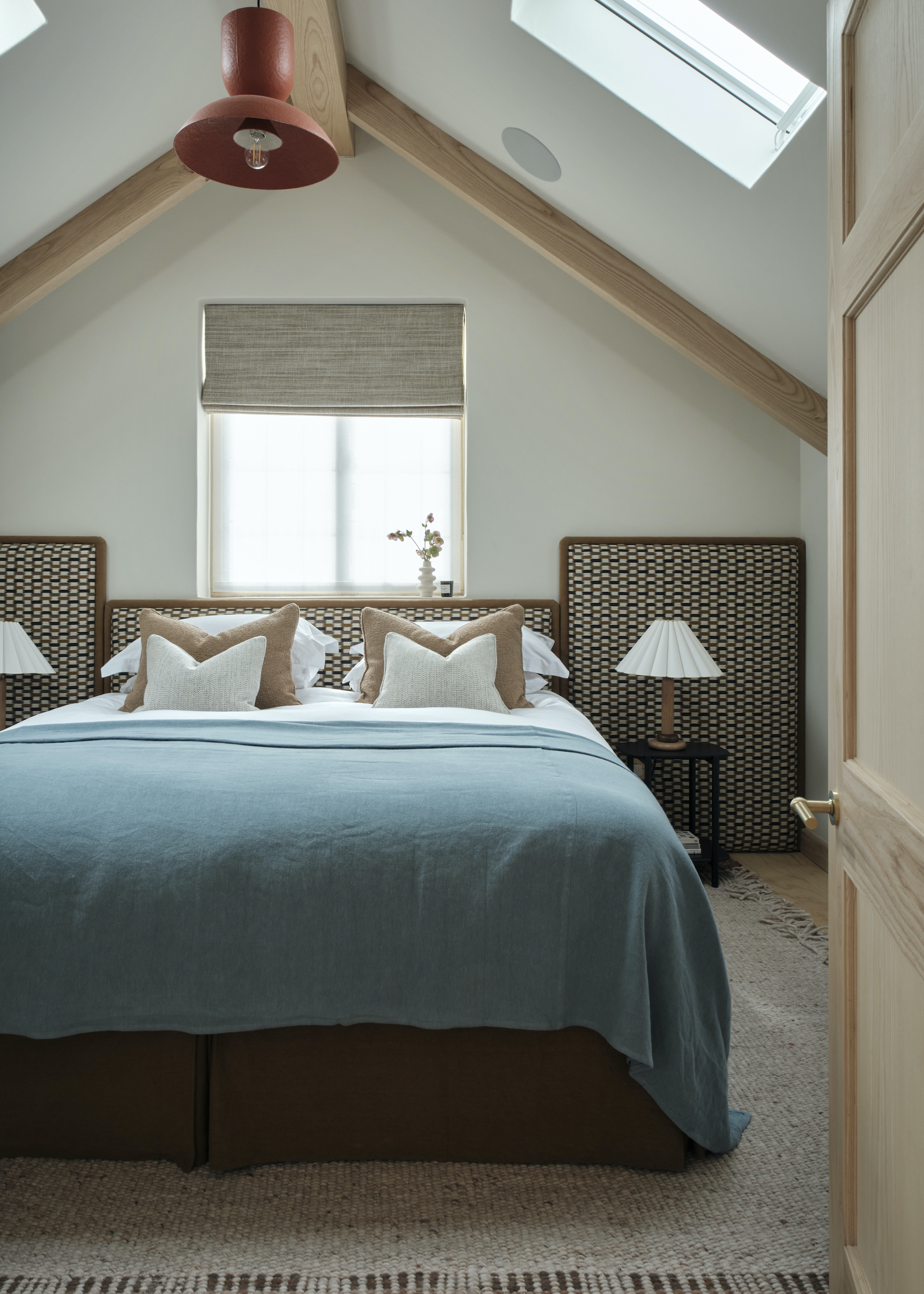 loft conversion with bed and upholstered headboard and wood beams and metal light shade