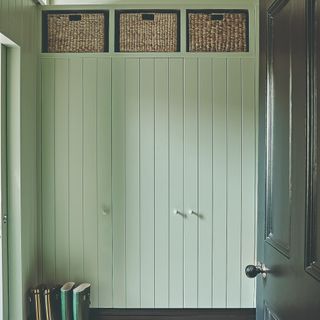 A sage green hallway with built-wardrobes and storage wicker baskets