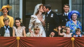 View of just-married couple Sarah, Duchess of York (center left), and Prince Andrew, Duke of York (center right), as they kiss on kiss the balcony of Buckingham Palace, London, England, July 23, 1986. Among those with them are Queen Elizabeth the Queen Mother (1900 - 2002) (right, in blue) and Andrew's brother, Prince Edward, Earl of Wessex (behind her).