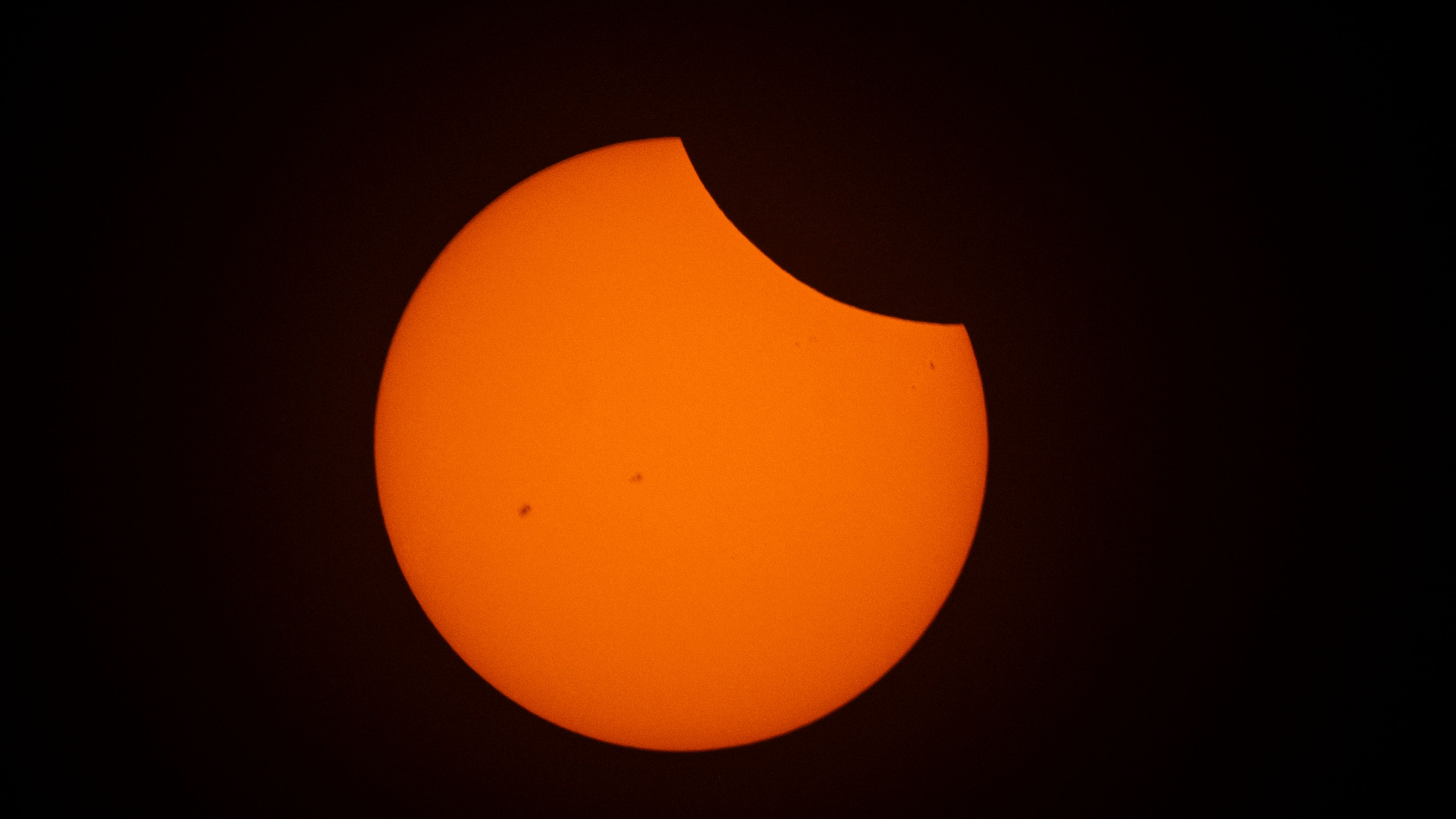 The moon's silhouette obscures the upper right of the sun's disk against a black sky during a solar eclipse.