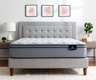 A plush mattress on a grey bed frame against a white bedroom wall.