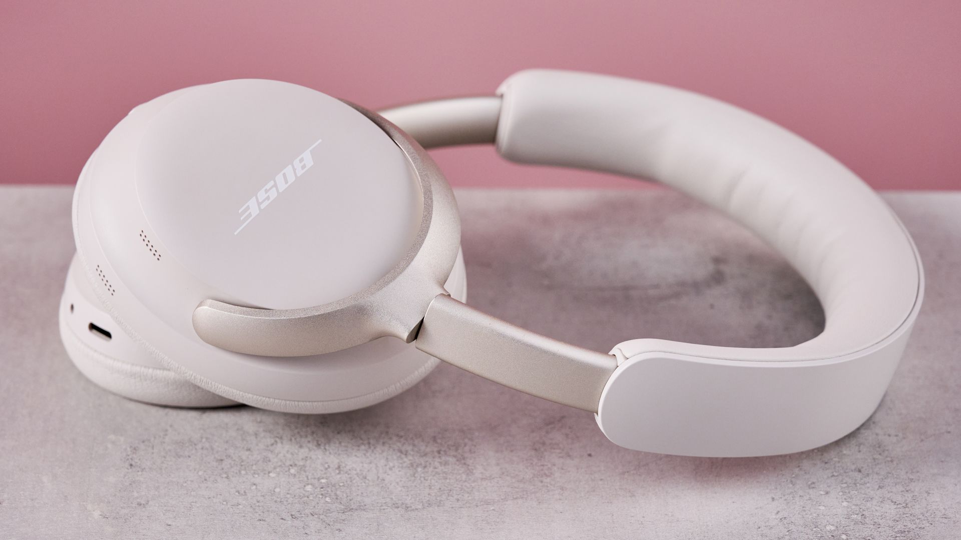 Bose QuietComfort Ultra Headphones on a gray surface with a pink background