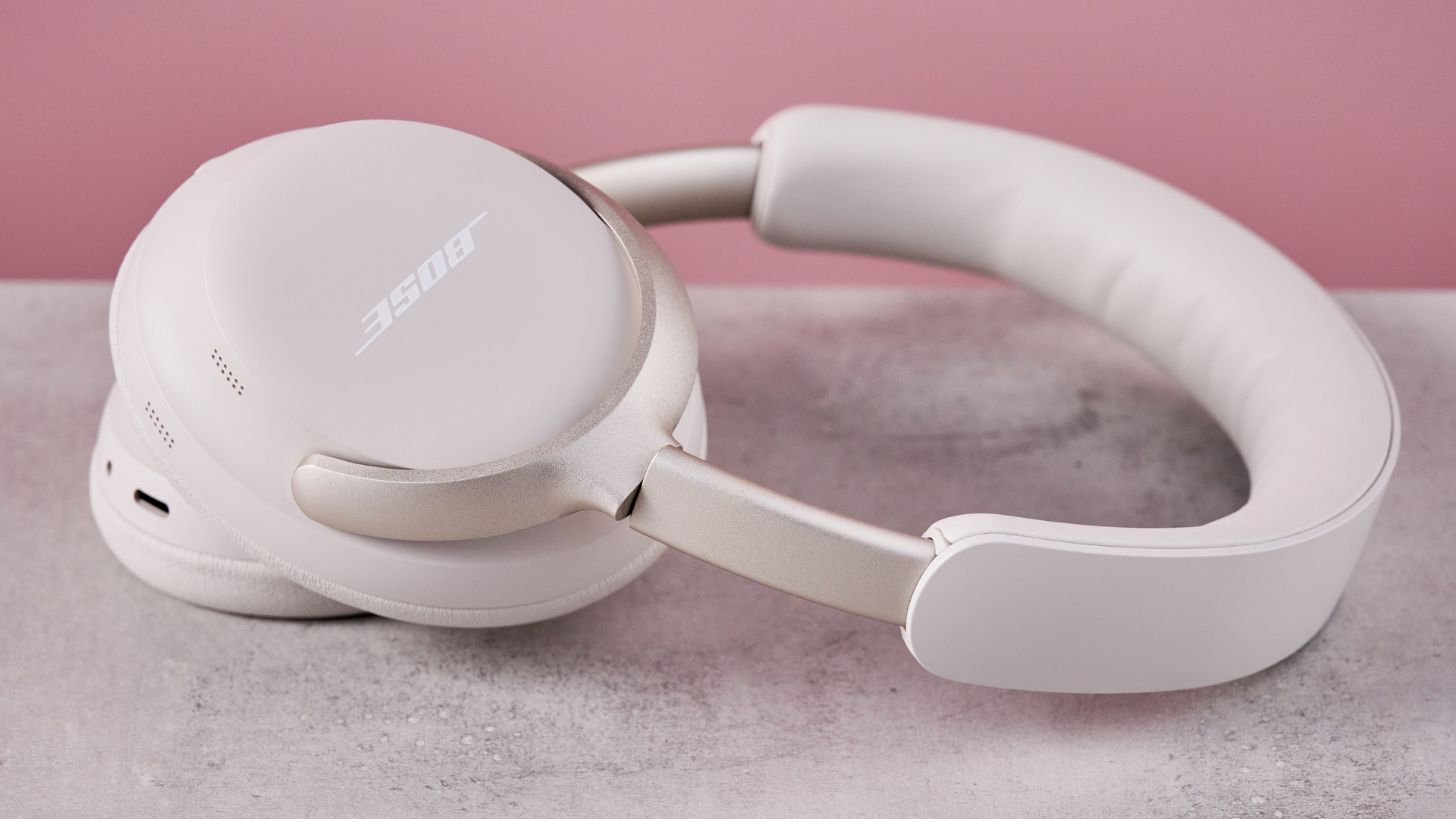 Bose QuietComfort Ultra Headphones on a gray surface with a pink background