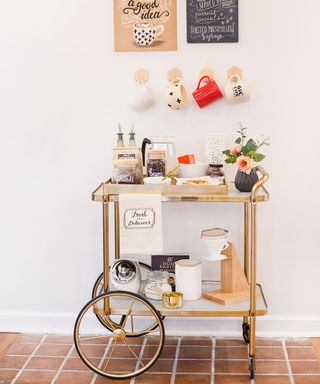 Glam DIY coffee bar trolley in gold finish, styled with personalized picks, flowers, and complemented by hanging mugs on wall and washi taped prints
