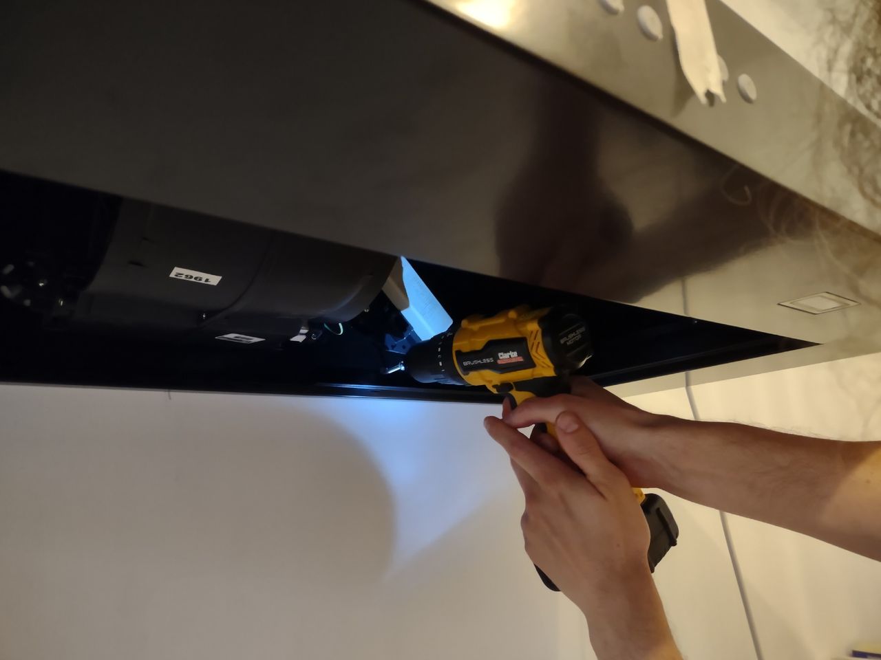 A black pyramid chimney cooker hood being fixed to a white kitchen wall with a power tool
