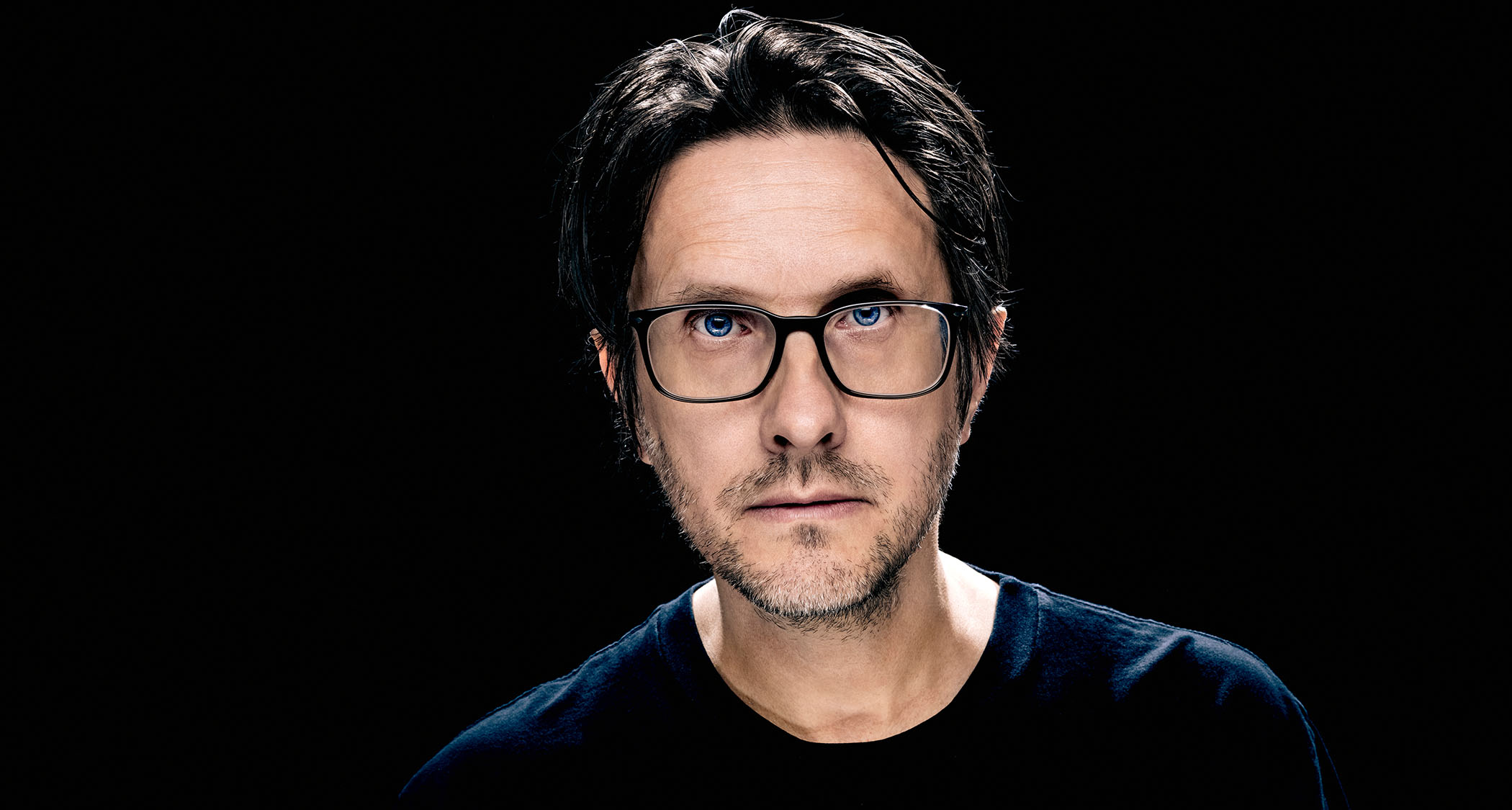 A portrait of Steven Will in close-up against a black background